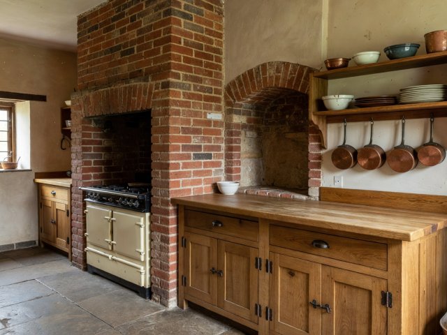 Cottage kitchen layout with range cooker recessed into brick chimney breast and timber prep run beside it