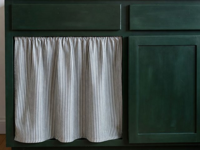 Hand-painted deep green cottage base cabinet paired with a pleated ticking stripe linen curtain under the sink